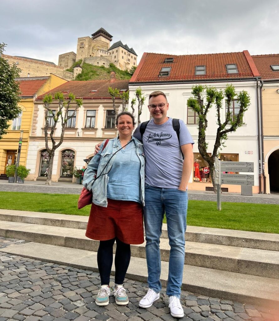 Zwei Personen auf einem Marktplatz mit einer Burg im Hintergrund.
